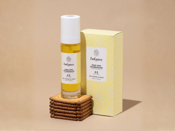 Huile nourrissante Enfance Paris pour visage et corps, adaptée dès la naissance, contenant une bouteille avec un liquide clair.